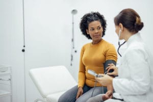 Doctor measuring blood pressure to a smiling woman in primary care clinic