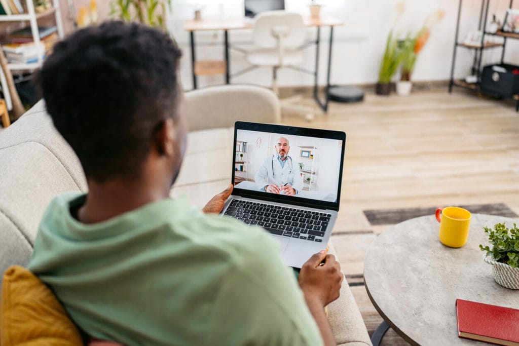 Man Having A telehealth appointment On The Laptop On The Sofa