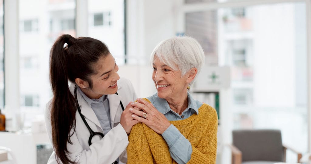 Happy, hug and face of a primary care doctor with a woman providing elderly care.