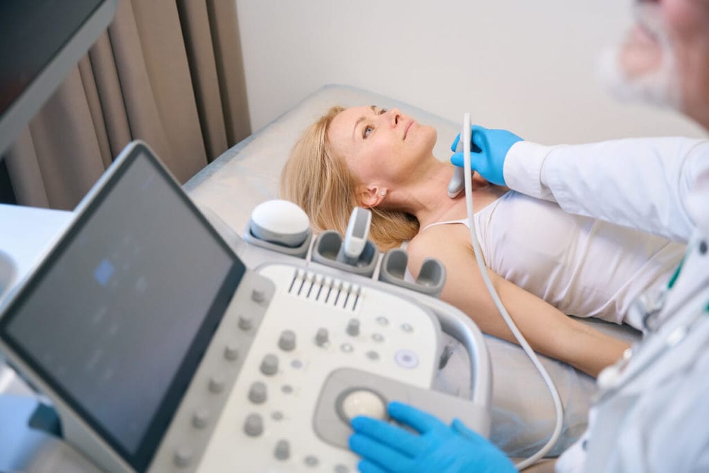 A woman is undergoing a thyroid ultrasound exam at a clinic.