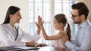 Smiling female family practice doctor is giving a high five to a child patient who is with her dad at the clinic.