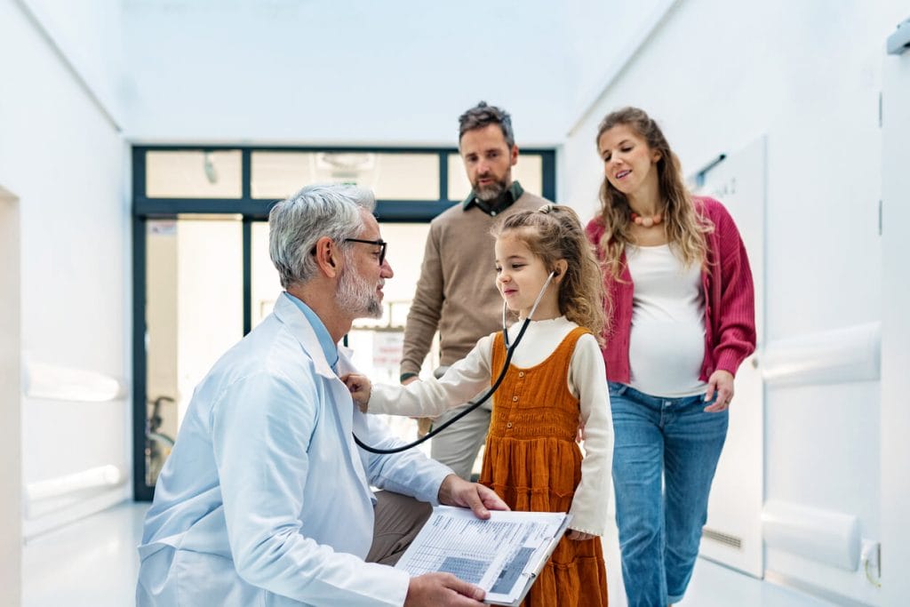 A family practice physician listens to a girl's heartbeat using a stethoscope during an examination in a modern clinic with her parents.