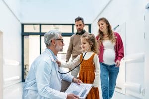 A family practice physician listens to a girl's heartbeat using a stethoscope during an examination in a modern clinic with her parents.
