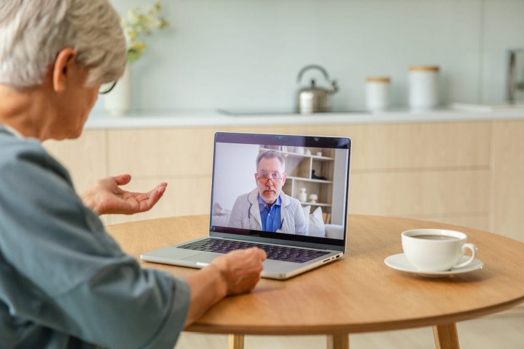 A senior male doctor, who is an expert in his field, is conducting an online examination of an older woman through telemedicine.