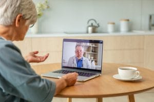 A senior male doctor, who is an expert in his field, is conducting an online examination of an older woman through telemedicine.