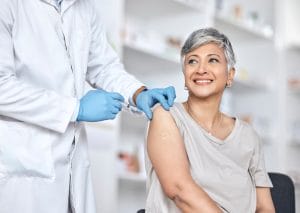 A happy female senior patient is being attended to by a medical professional while receiving her vaccination.